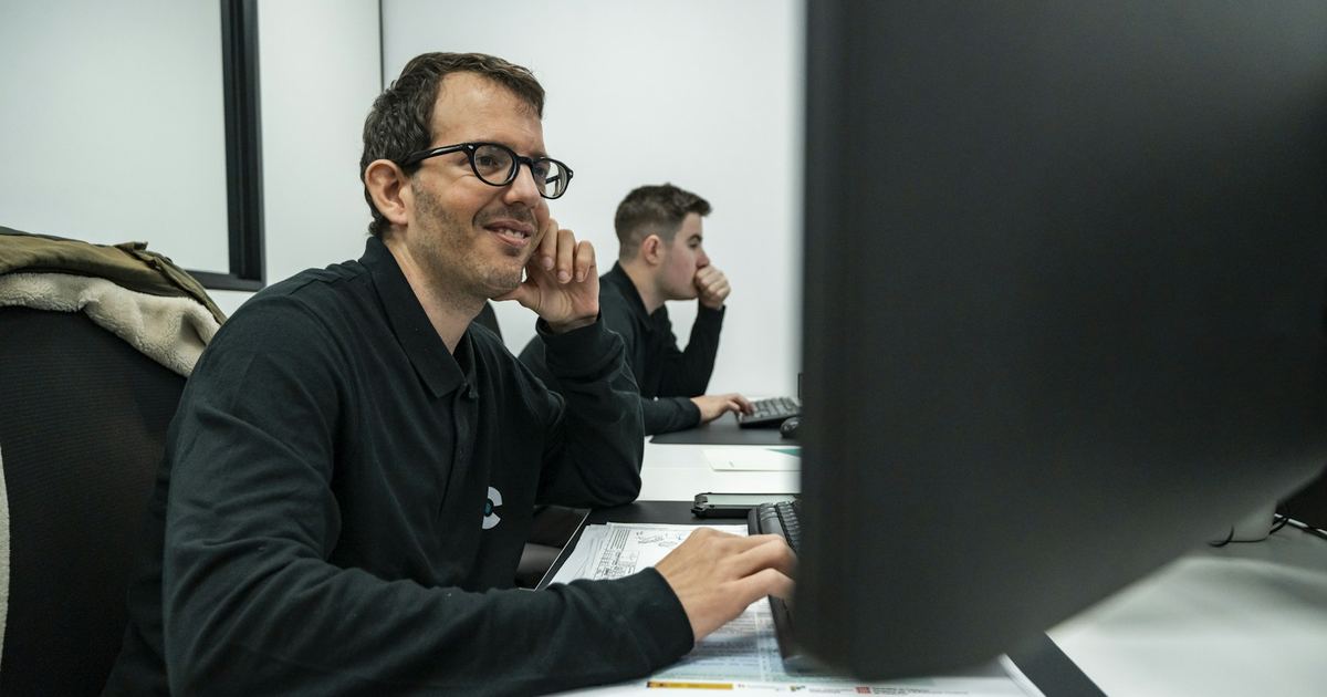 Un expert souriant à son poste de travail, un collègue derrière lui